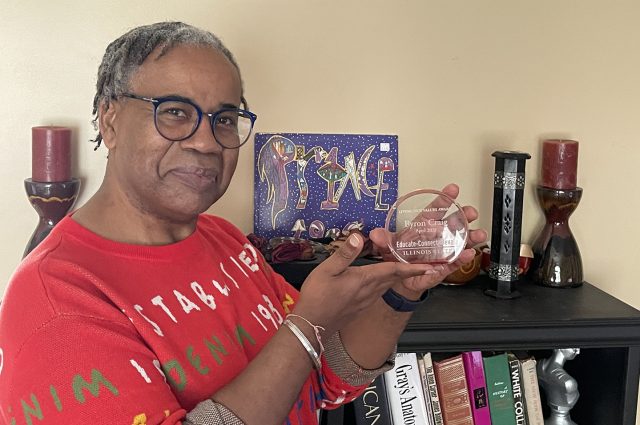 Dr. Byron Craig standing in front of a bookshelf holding an award.