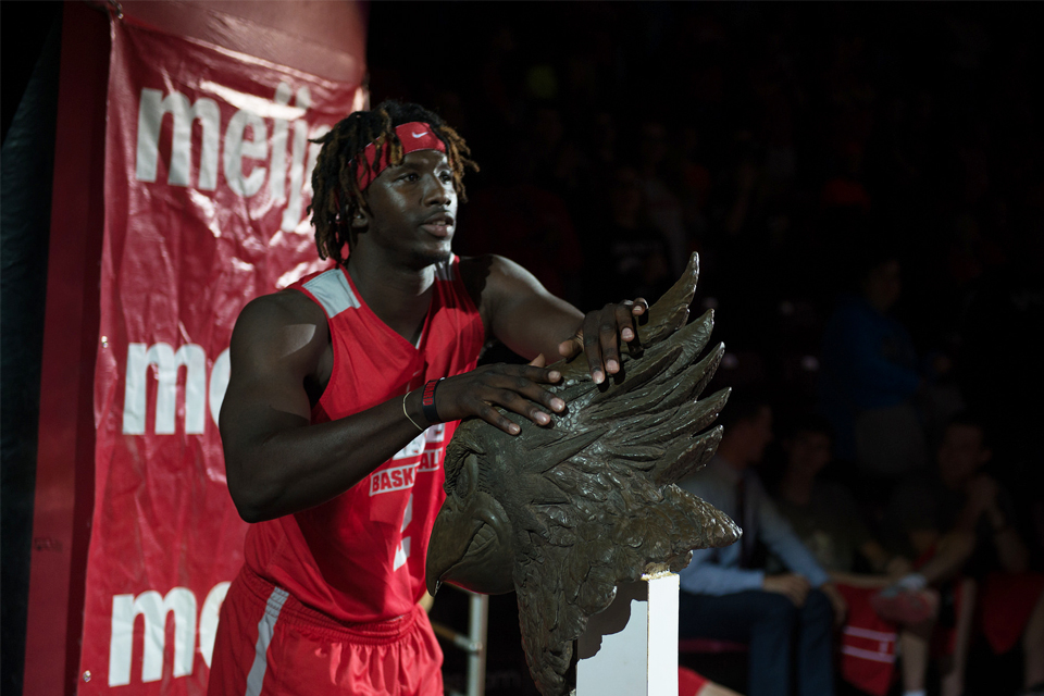 Basketball player touching bust of Reggie Redbird