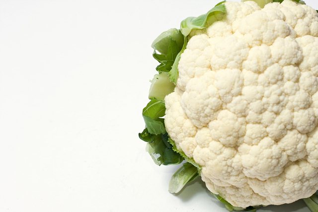Part of a white cauliflower with leaves on the side