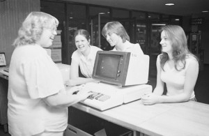 Circulation staff member stands at computer with three students on other side of desk.