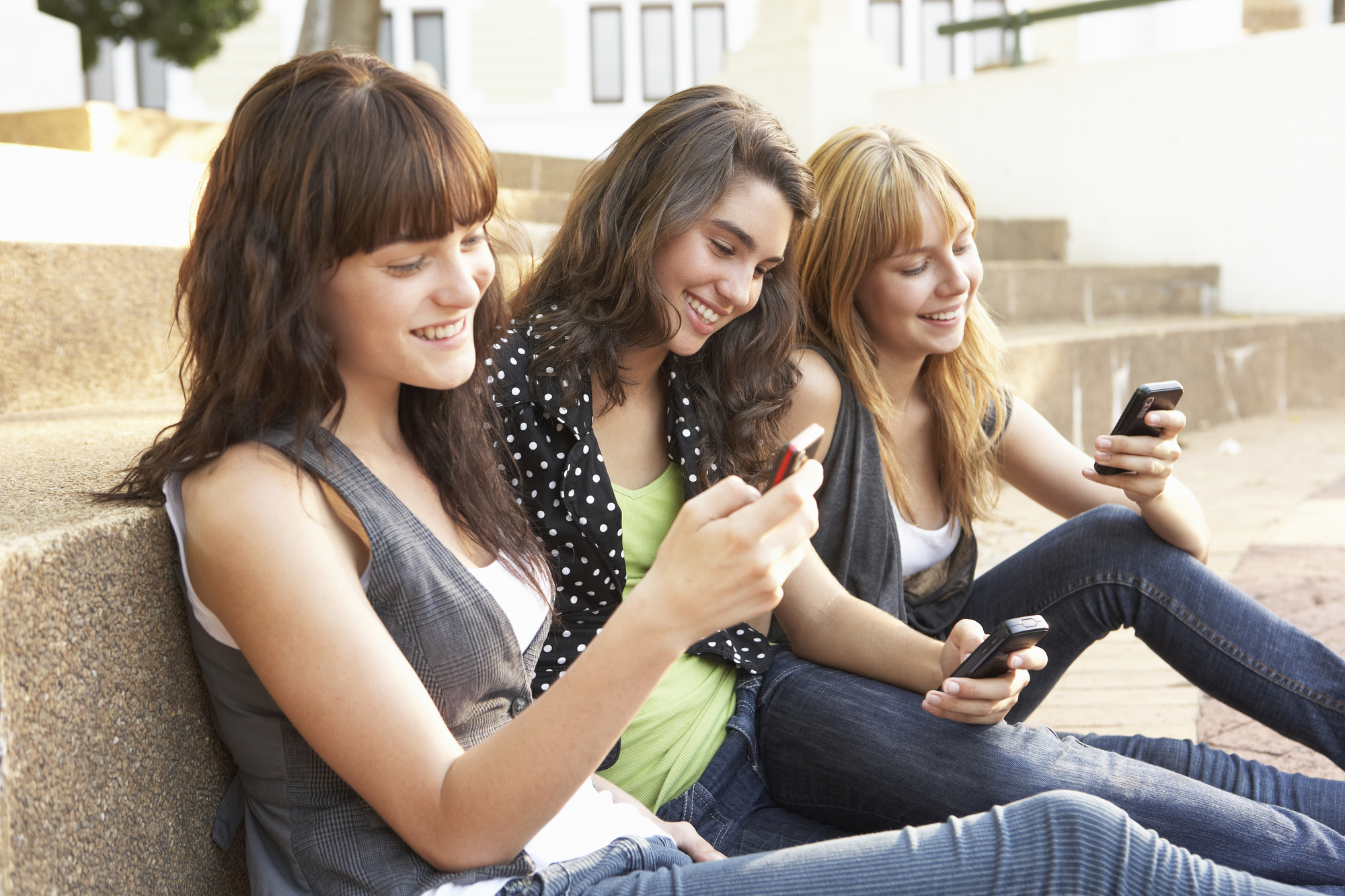 image of Group Of Teenage Students Sitting Outside On College Steps Using Mobile Phone