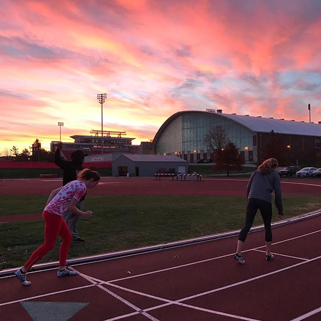 Two sprinters preparing to run on the track with a sunset over Horton Fieldhouse in the background