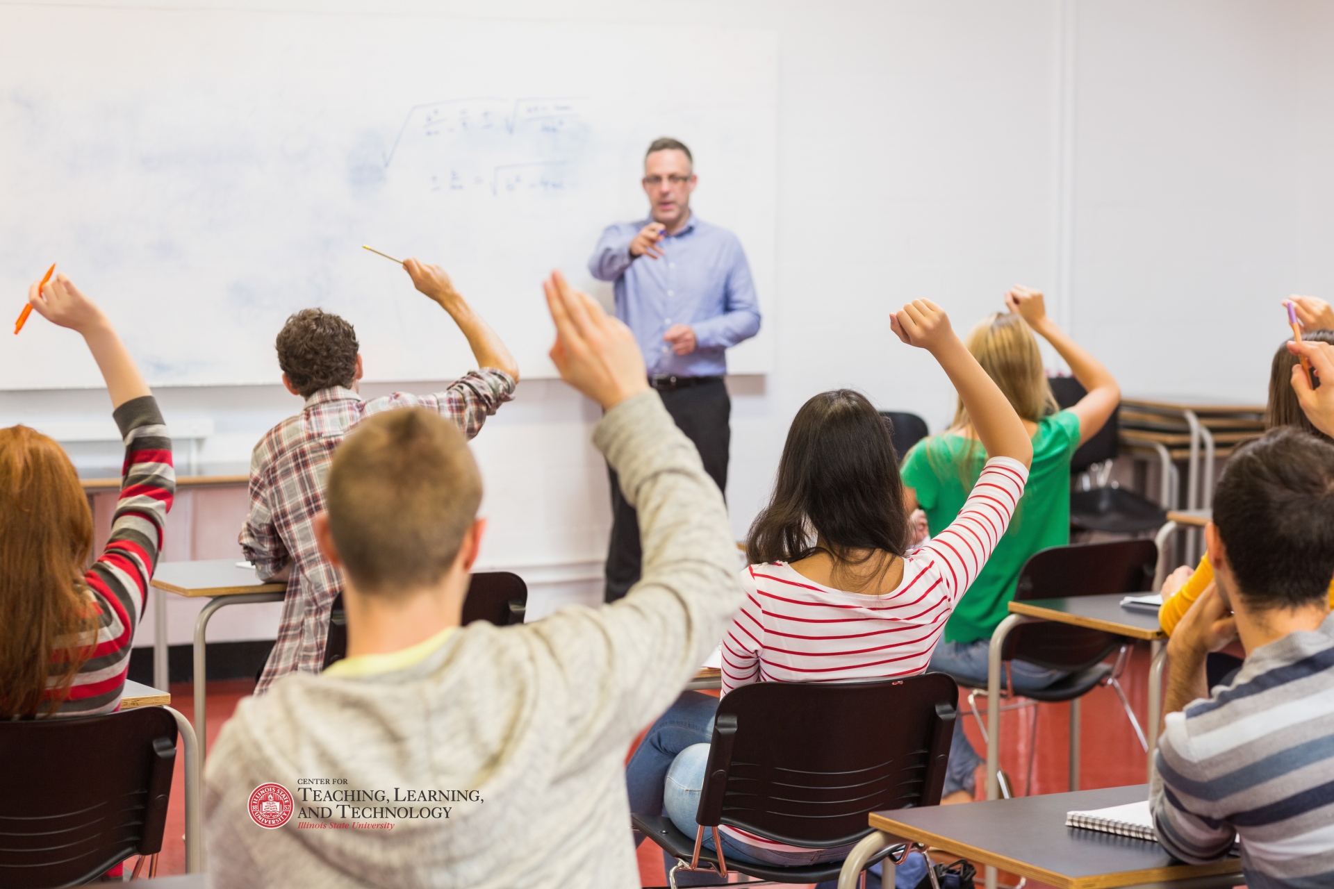 Teacher in front of class, student with raised hands