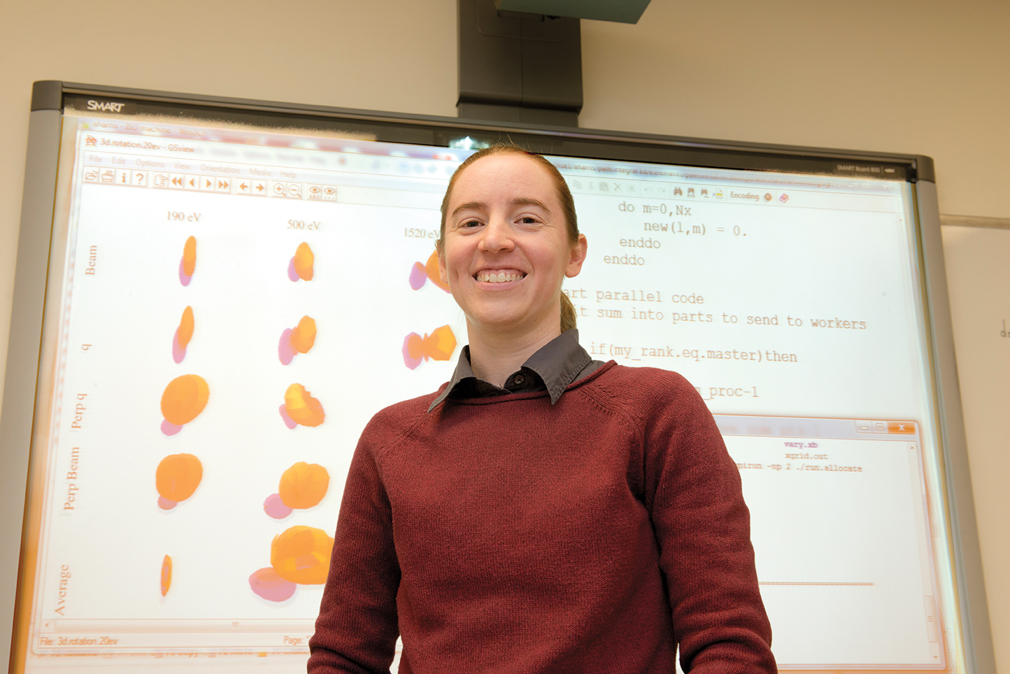 Illinois State Physics Professor Allison Harris standing in front of a whiteboard containing her research.