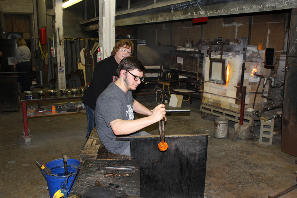 Tyler Wolf, senior art major, helps an alumna sculpt a glass paperweight at an alumni event.