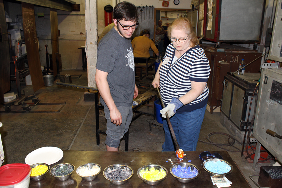 An alumna picks out colors for a glass paperweight with Tyler Wolf, a senior art major, at an alumni event.