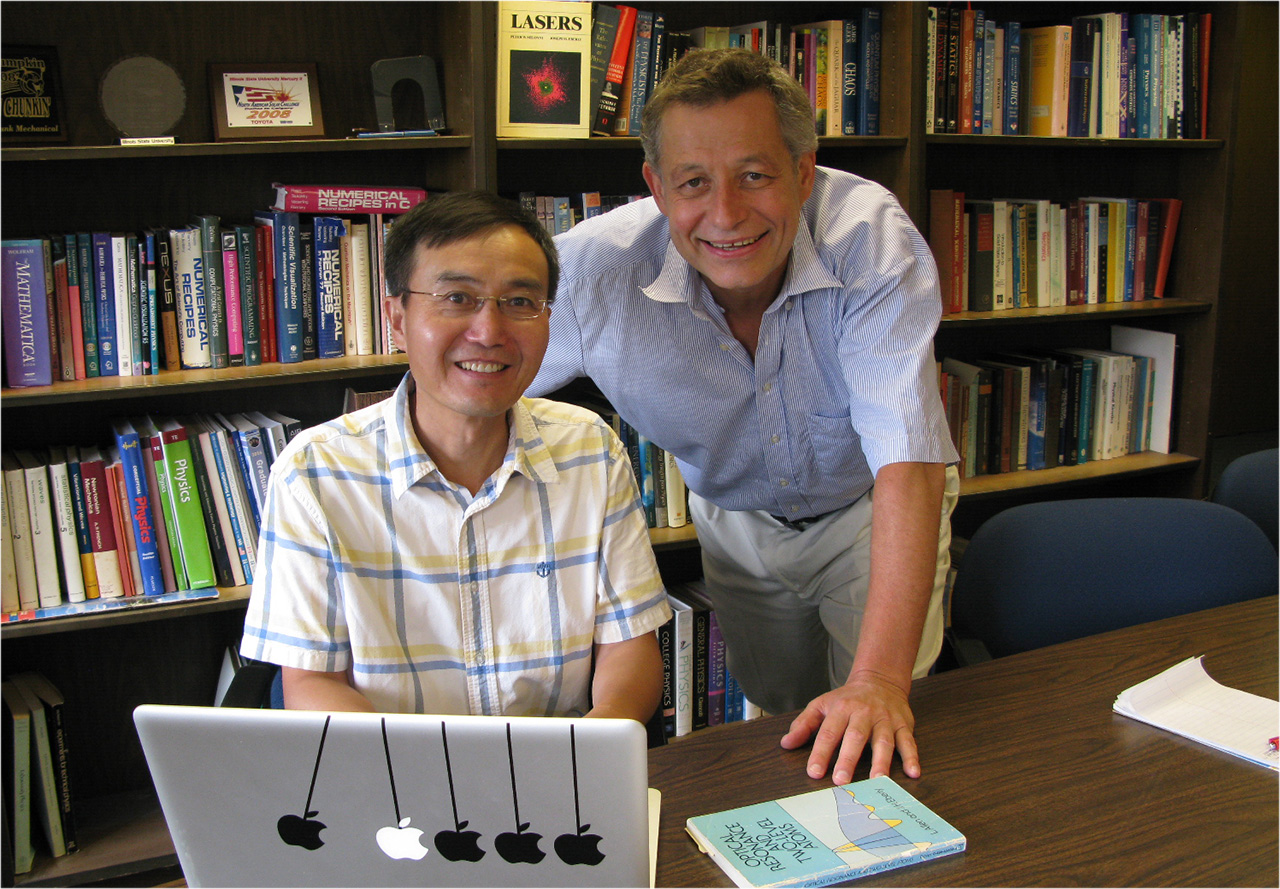 Professors Q. Charles Su and Rainer Grobe work at a laptop in front of rows of books