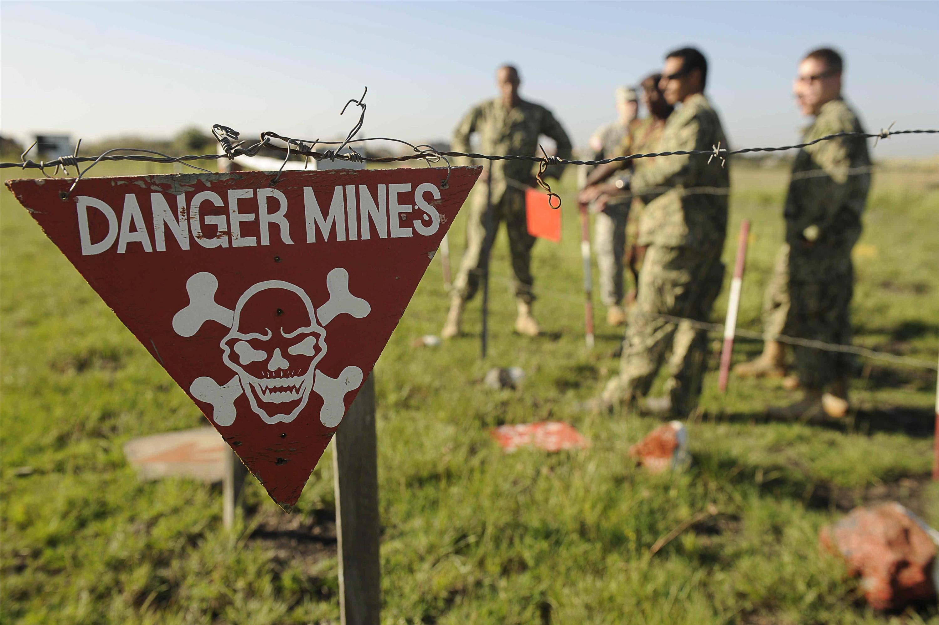 sign warning of landmines with soliders in the background.