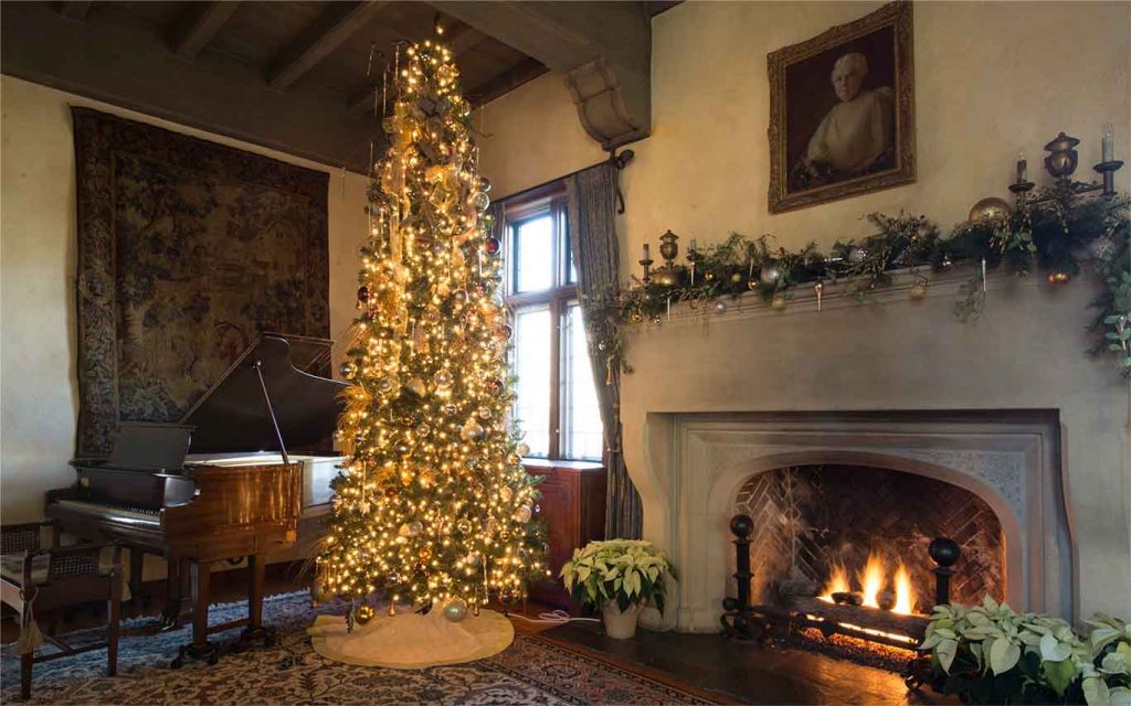 christmas tree near a grand piano and fireplace covered in garland and ornaments