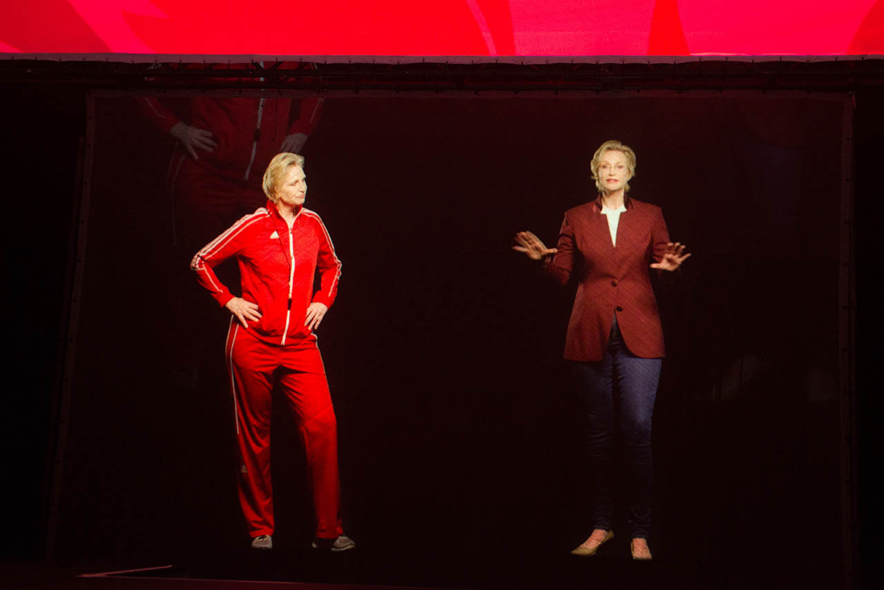 Jane Lynch ’82 appearing as a hologram on stage alongside “Sue Sylvester,” Lynch’s character from Glee.