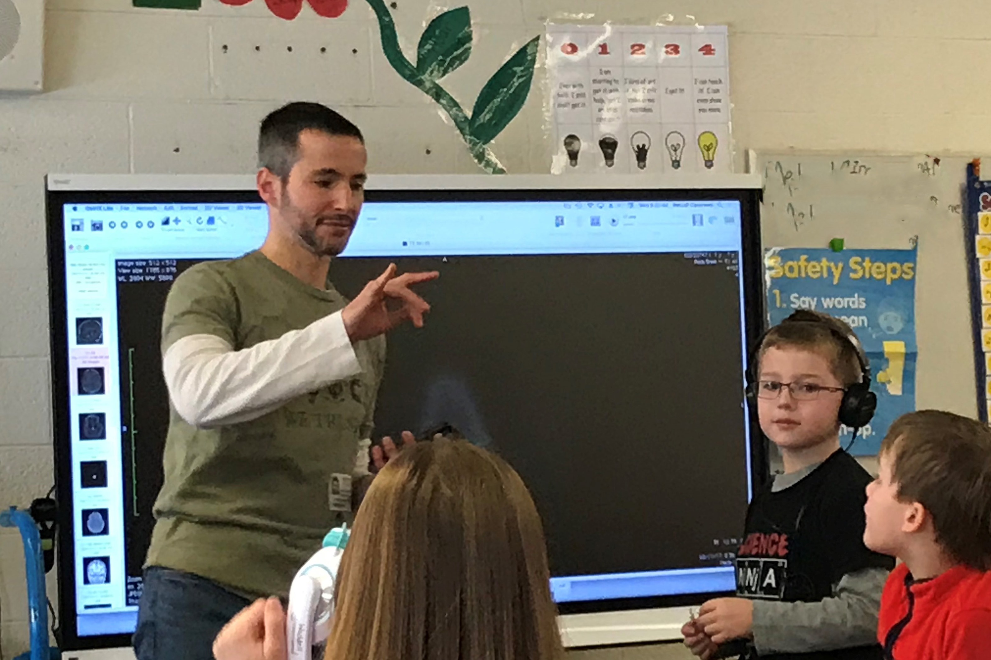 Jeff Wagman, Ph.D., PSY presents a short course on perception and the brain to second graders at Thomas Metcalf School. Connor Wagman, wearing headphones, helps with the demonstration.