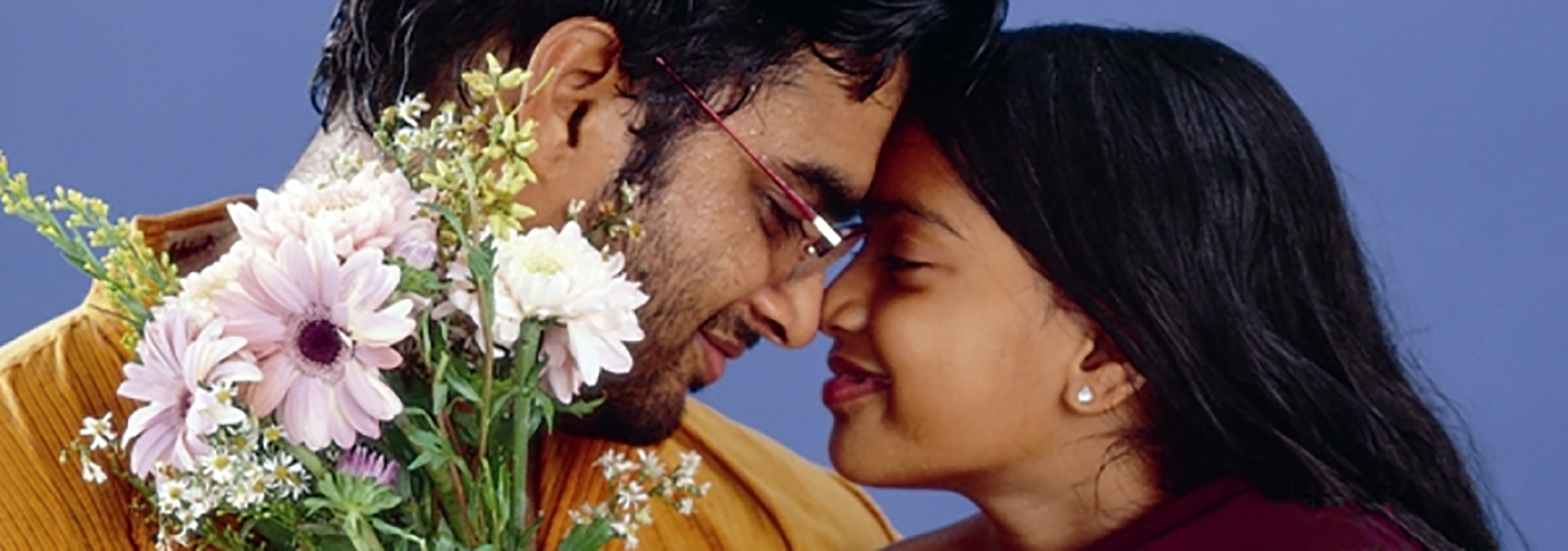 Man holding flowers and leaning his forehead to a smiling woman.