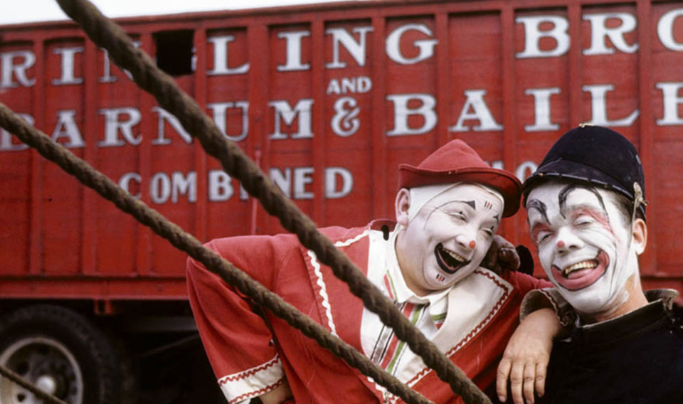 Two clowns in front of a baggage wagon