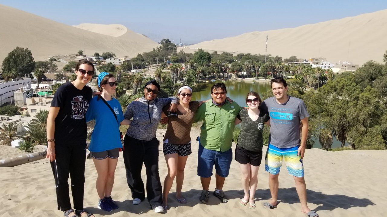 Group picture of students standing in front of an oasis in the desert, all are smiling.