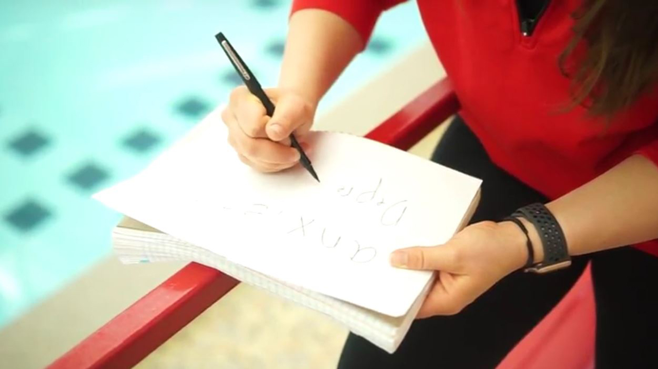 woman writing on a pad of paper with only the pad, her hands and her arms in focus.