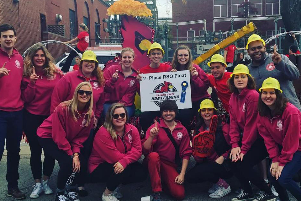 group of students with parade float and Redbird cutout