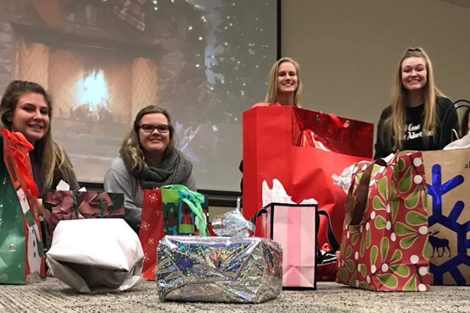 Four girls smile behind presents