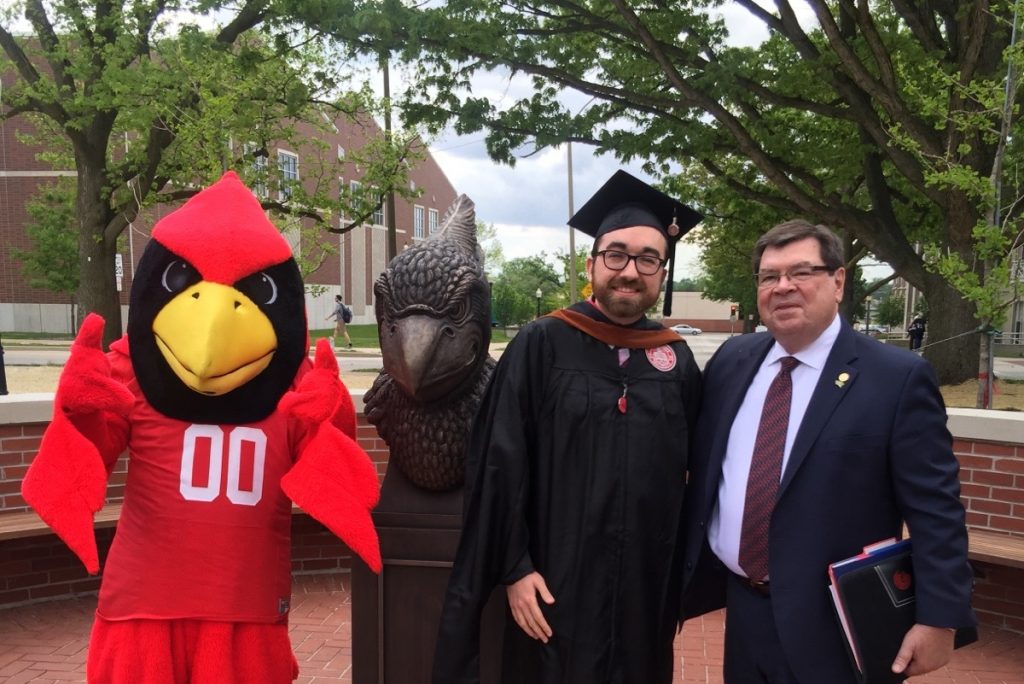 Reggie Redbird, student in cap and gown, and President Dietz posing in Redbird Plaza