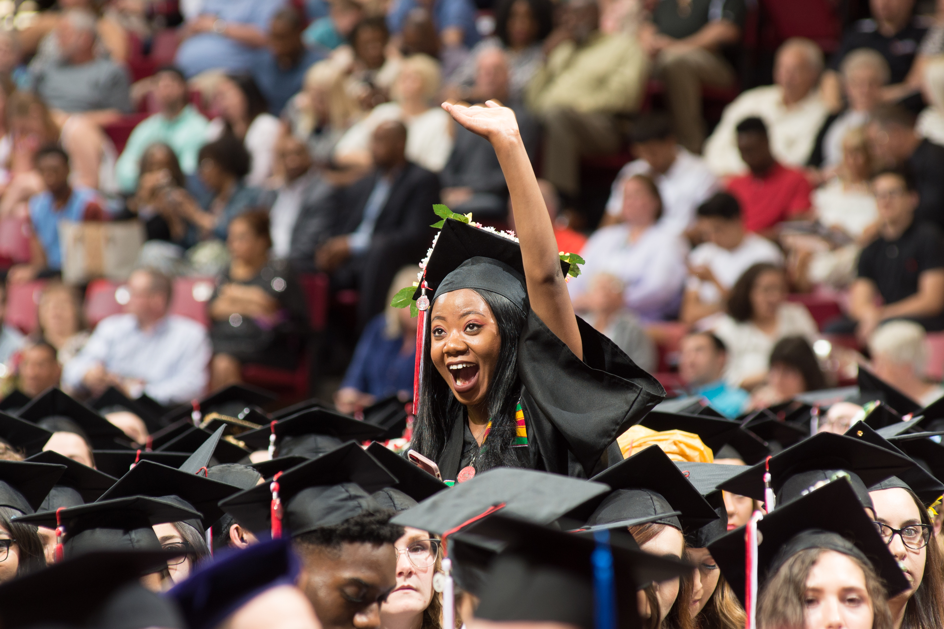 A graduate joyfully waves to someone in the crowd at Commencement