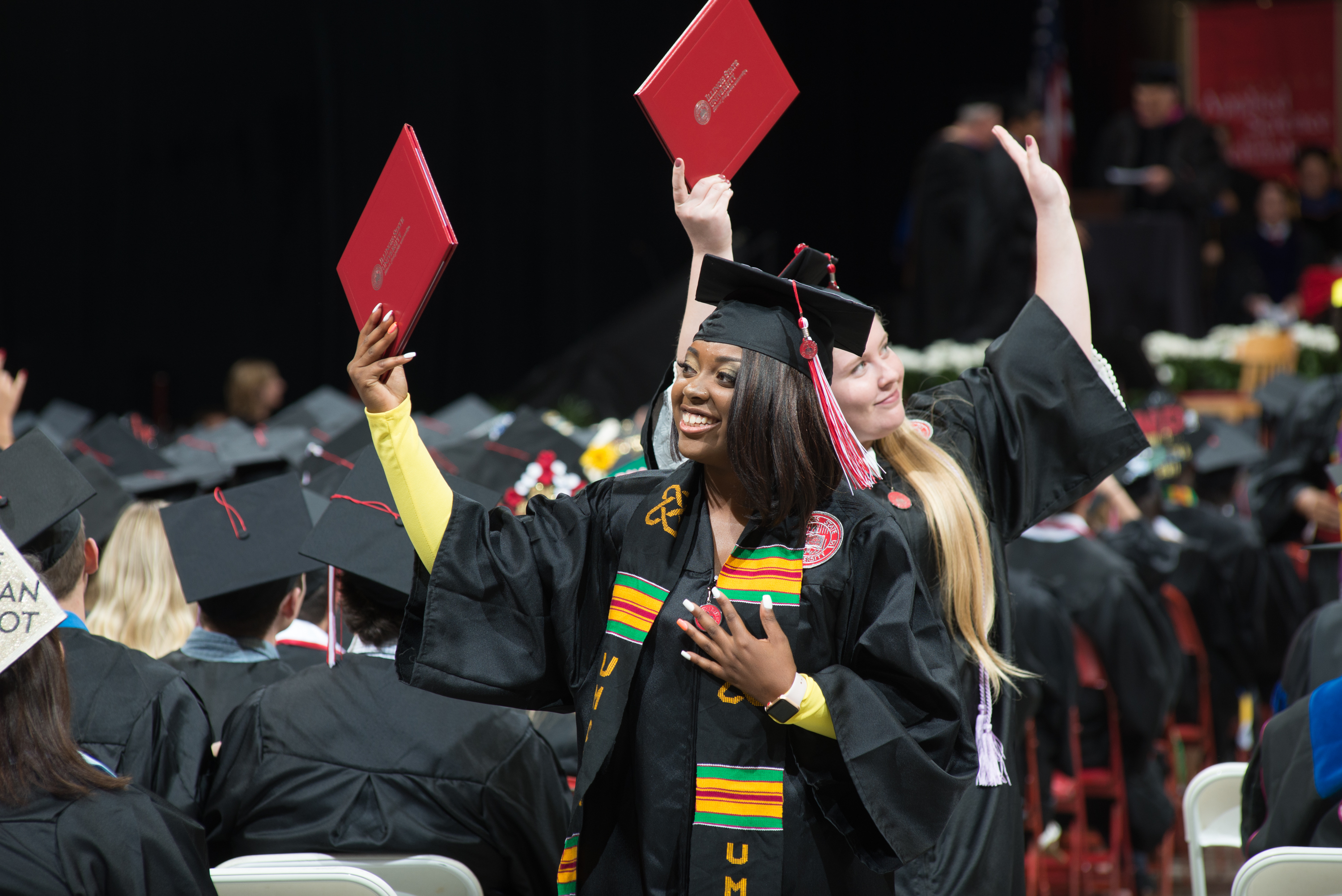 two graduates waving their diplomas in the air