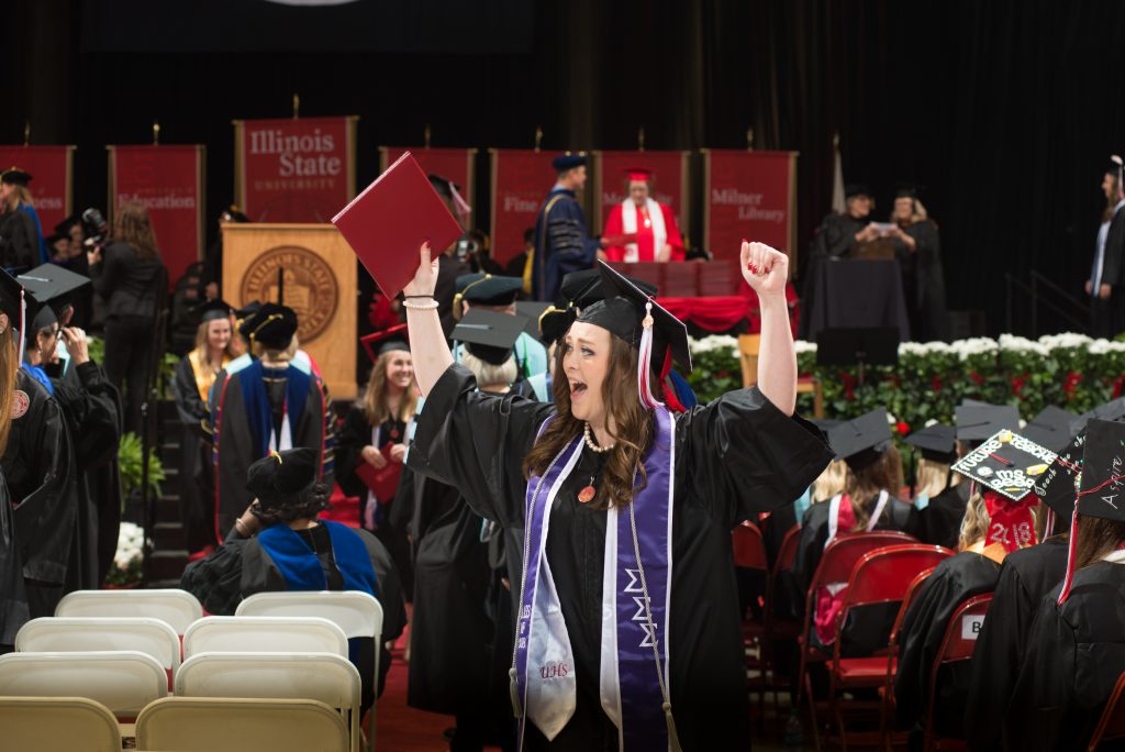 A graduate cheering with her arms in the air at commencement exercises