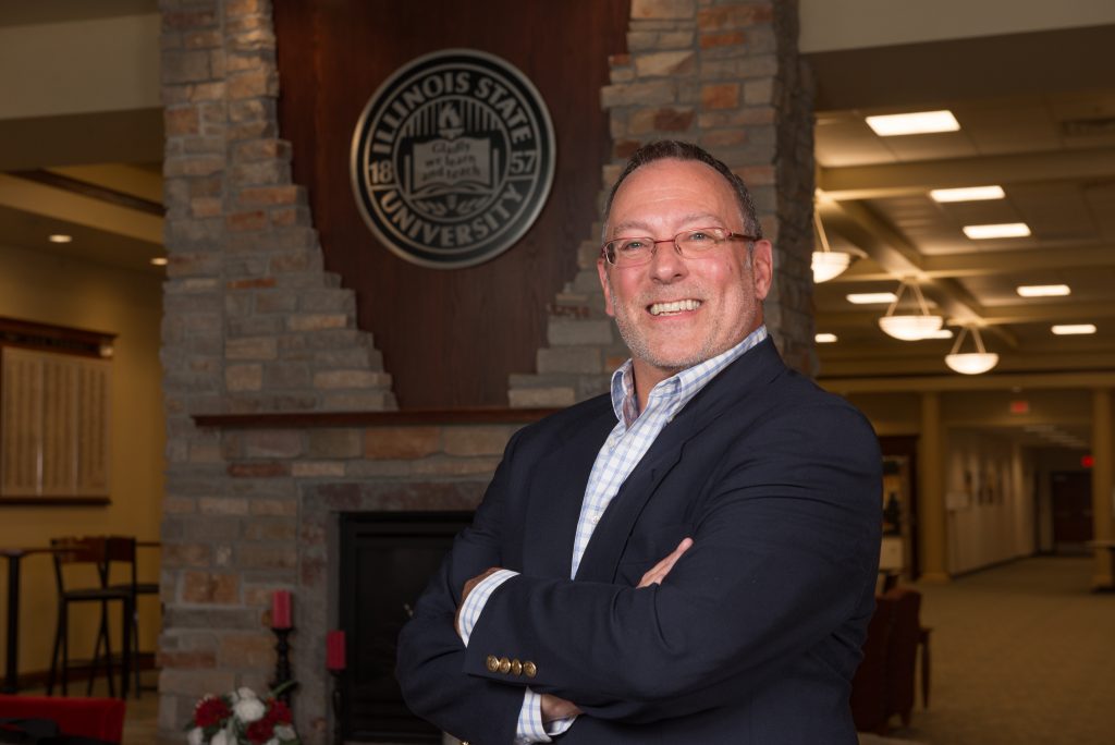 Ed Manley smiling in Alumni Center, in front of the ISU seal