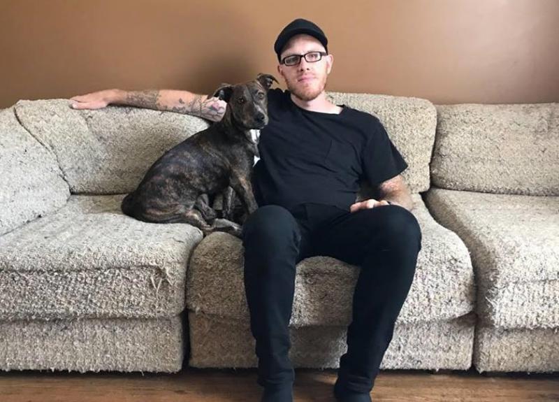 a man sitting on a couch with his arm on the back. a dog sits next to him