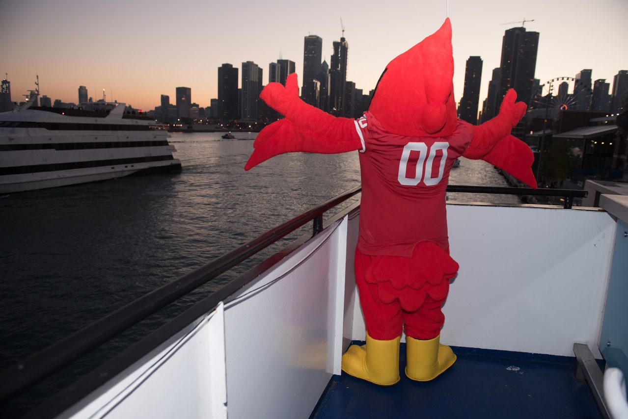 Reggie standing on a boat with back to camera, arms open with Chicago skyline in background.
