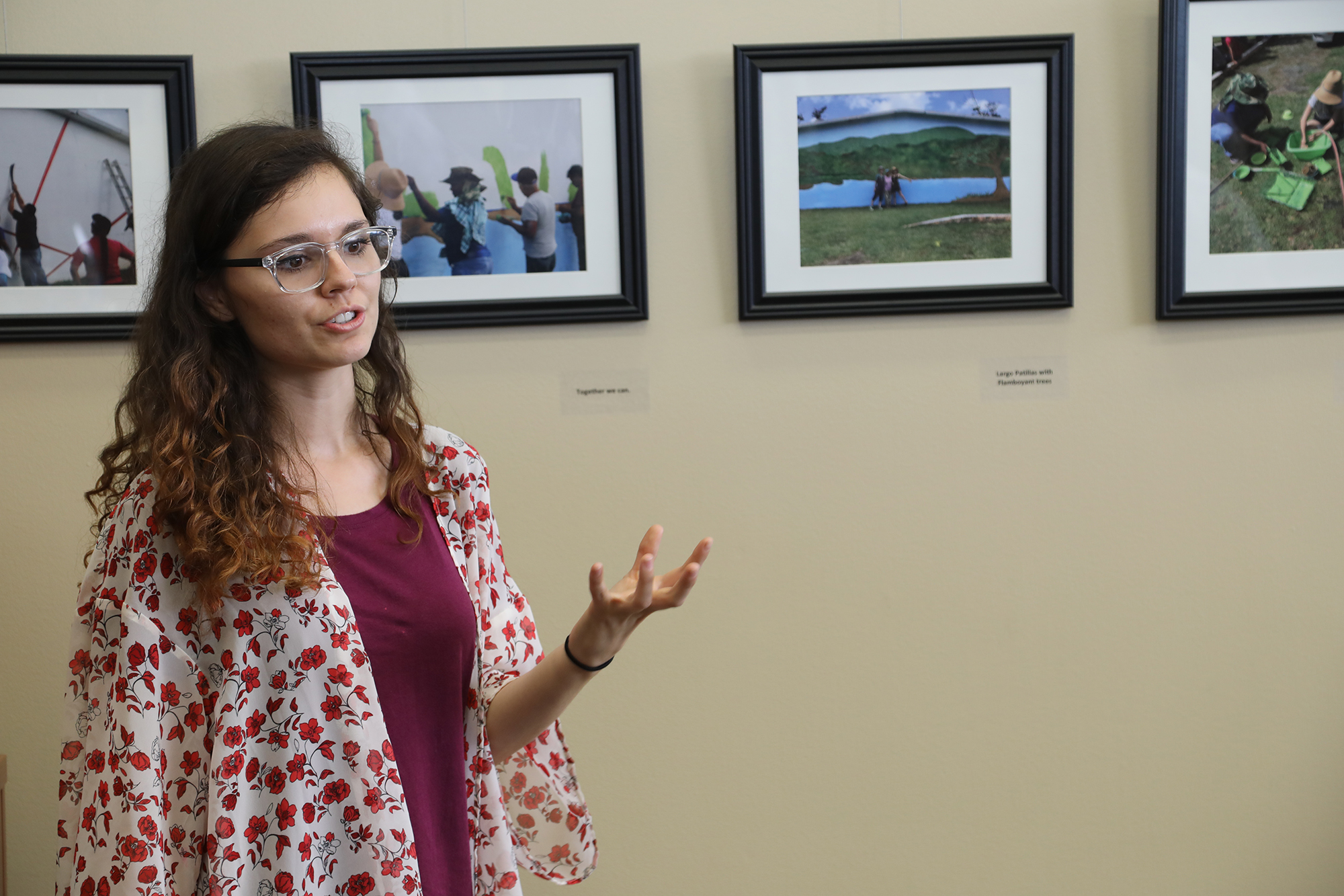 Woman speaking to others at an exhibit with pictures behind her