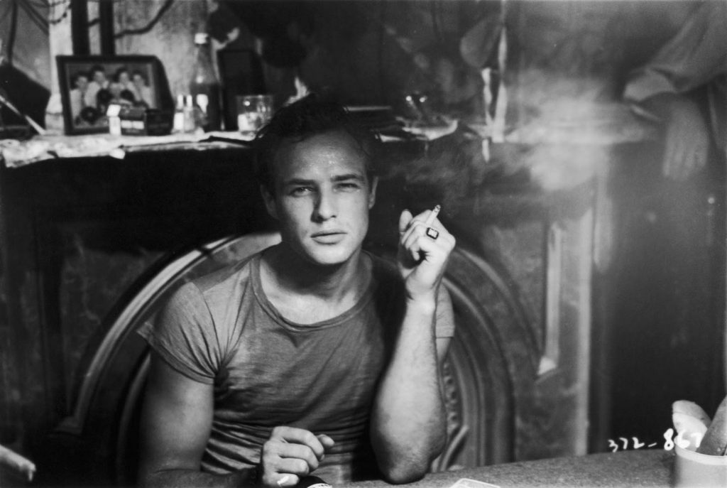 man sitting and smoking a cigarette with the smoke wafting around him,
