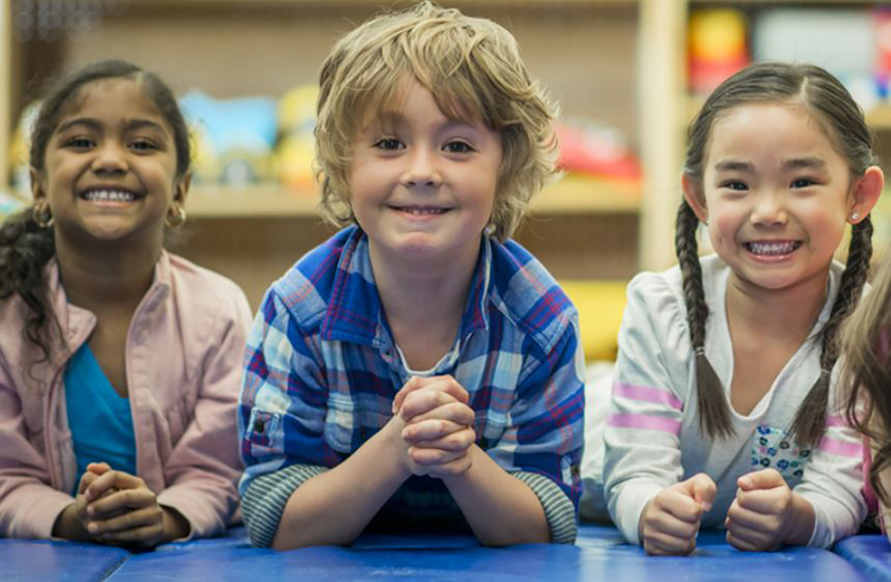 image of children smiling with elbows on a table
