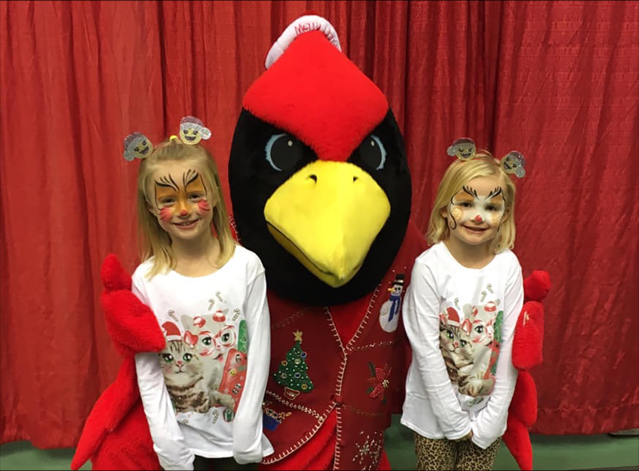 two face-apinted little girls posing with Reggie Redbird