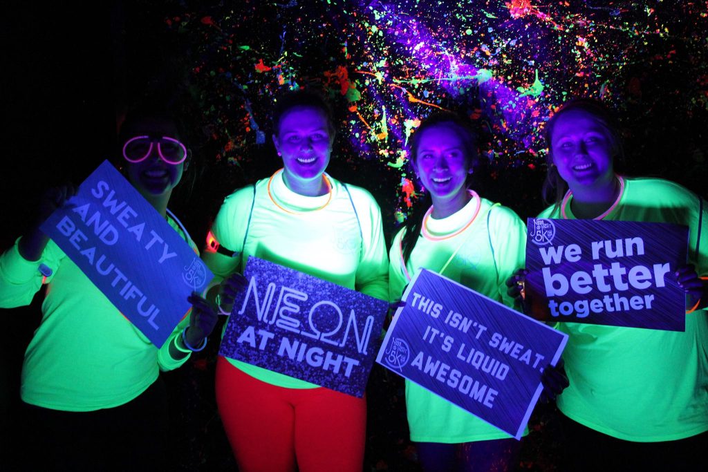 group of people holding signs at night for the neon fun run