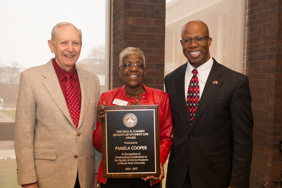 Three people smiling with middle person holding plaque