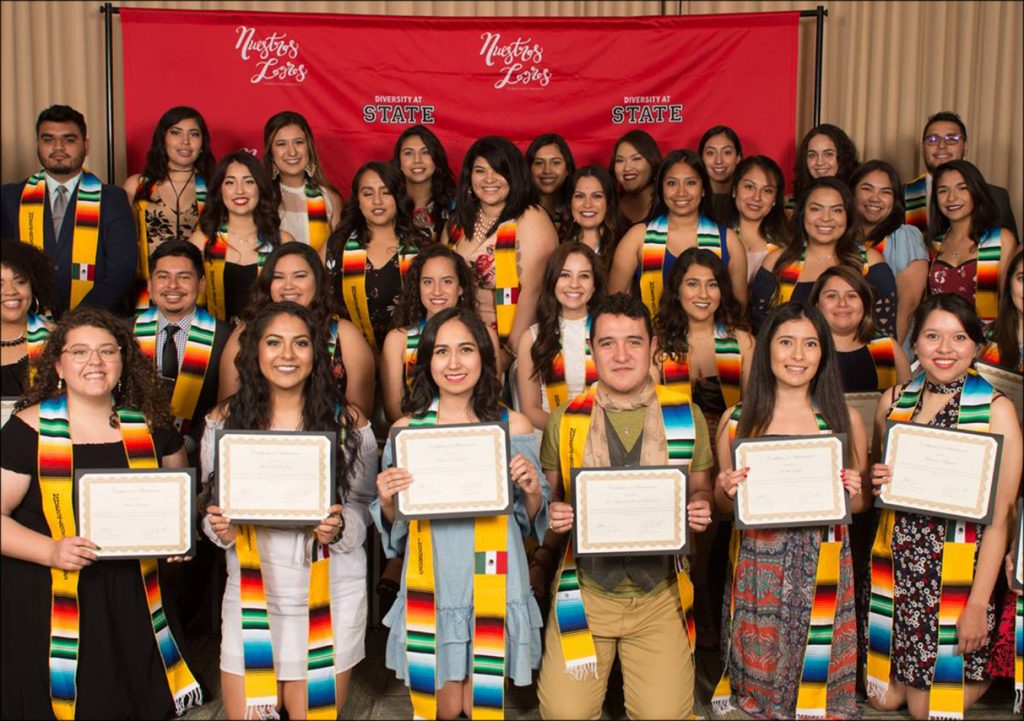 Students smiling and holding certificates and wearing graduation drapes