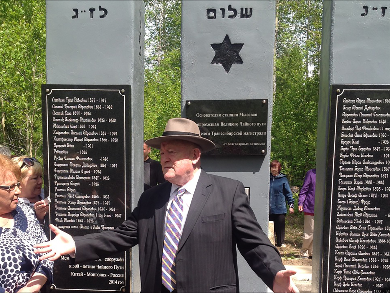 man standing in front of monunment with Star of David and plaques of names