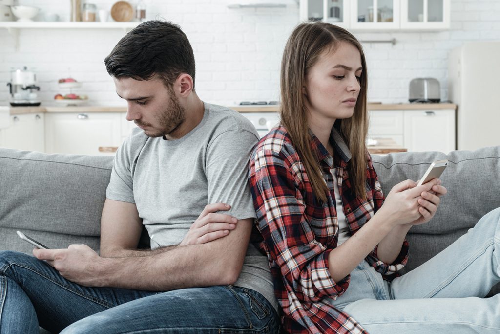 Unhappy couple ignoring each other using mobile phones. Boyfriend and girlfriend with smartphone addiction. Bad relationship concept