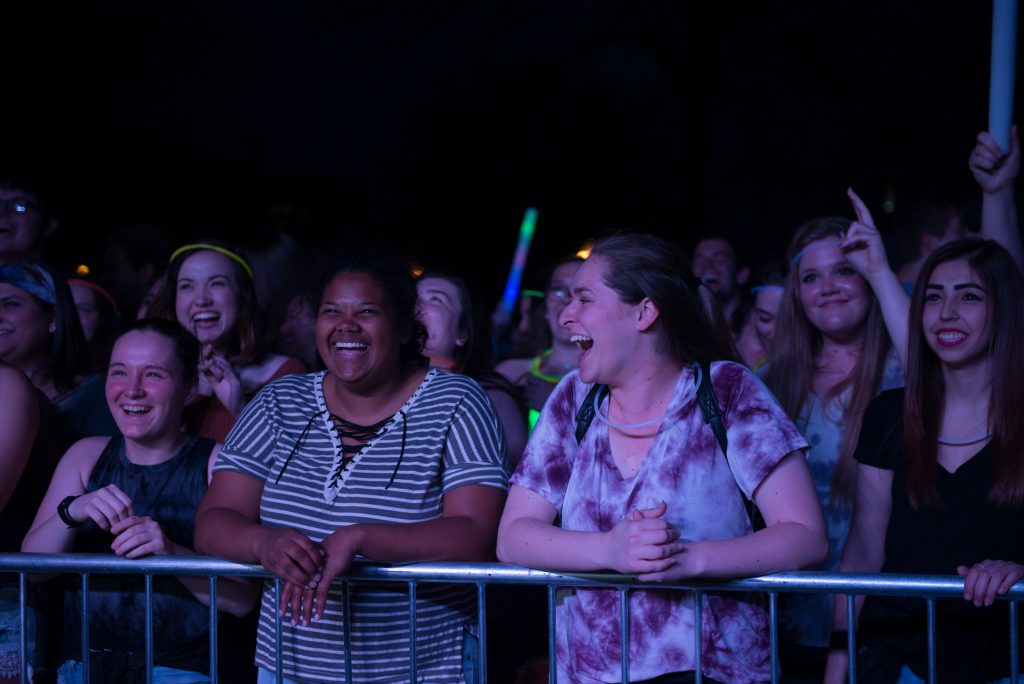 A group of students with glowsticks and big smiles enjoying a concert