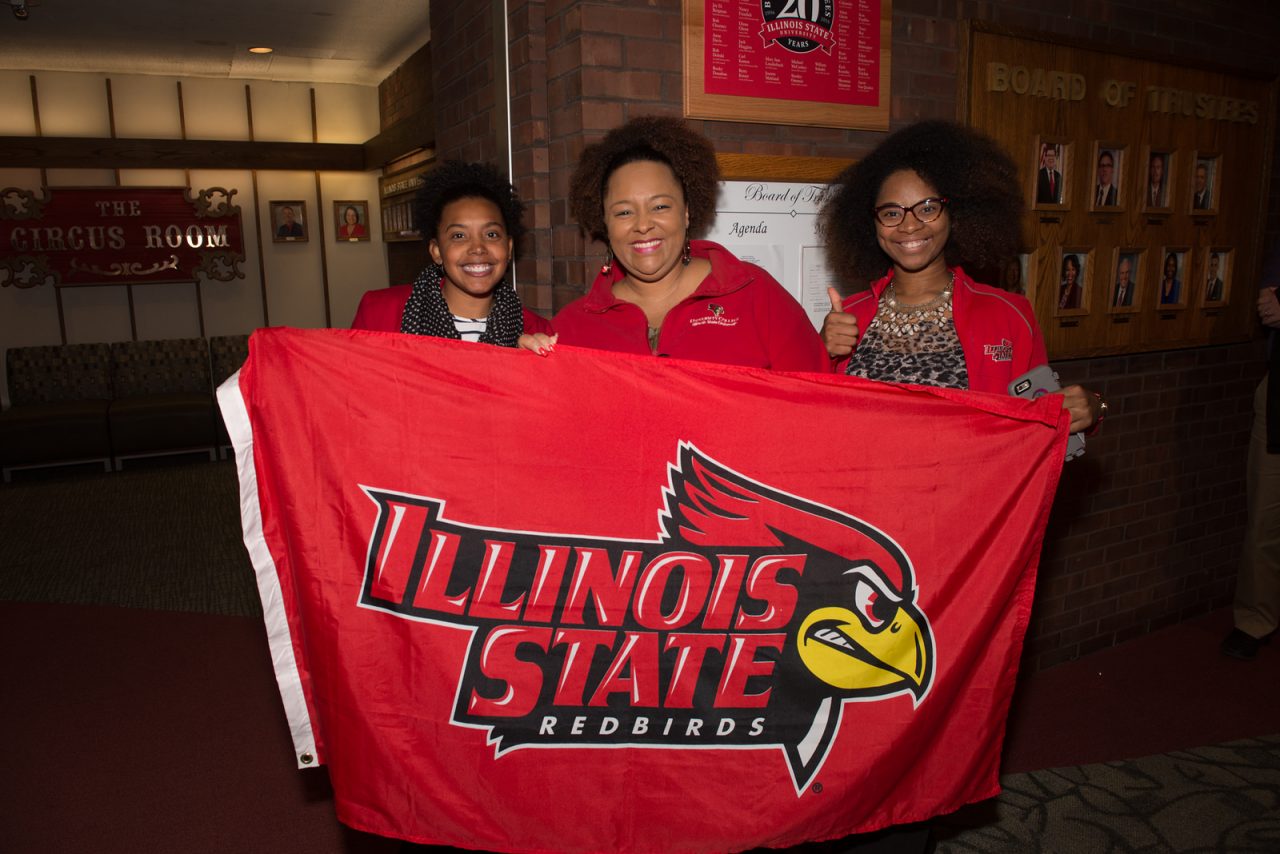 Three people holding a flag that has the words Illinois State Redbirds on it.