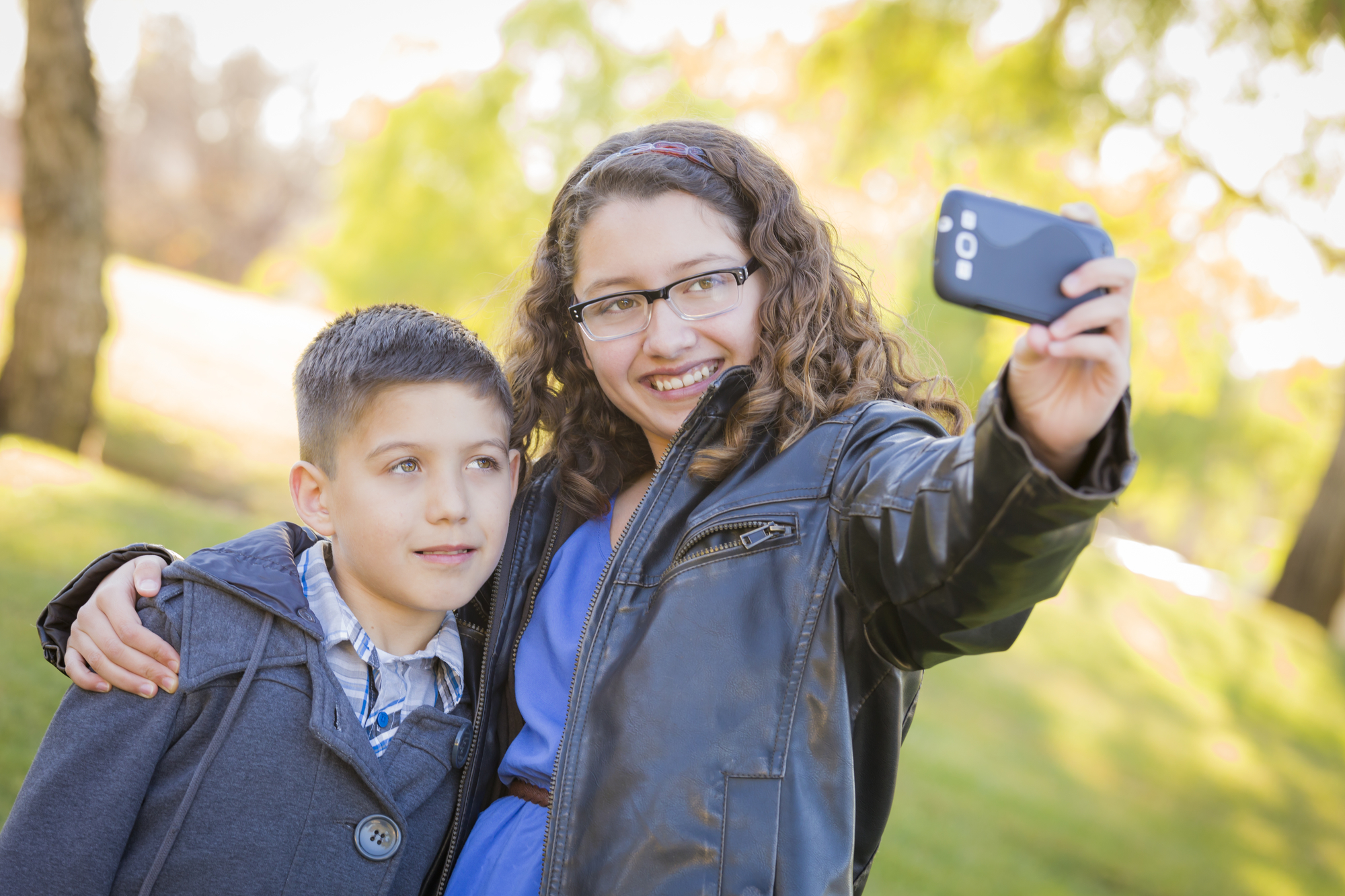 Brother and Sister Taking Cell Phone Picture of Themselves Outdoors At The Park.