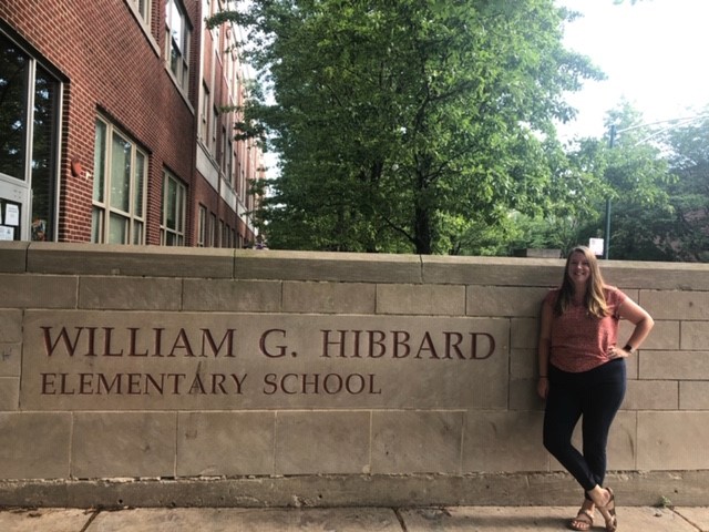 woman standing next to a sign that reads William G. Hibbard Elementary School