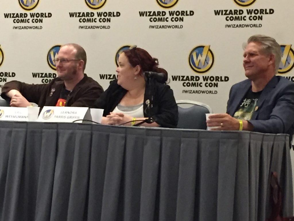 three people seated at a table with the Wizard World logo in the background