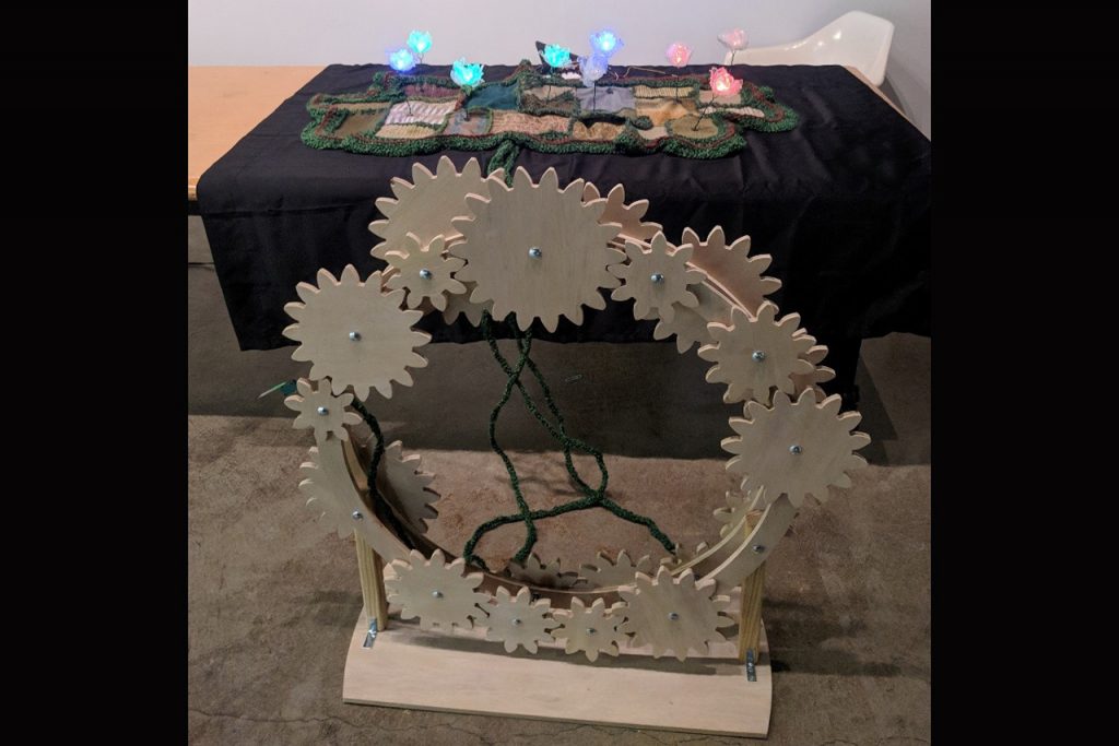 Image of the art piece Windstorm depicting wooden gears, topographic tapestry, and LED flowers.