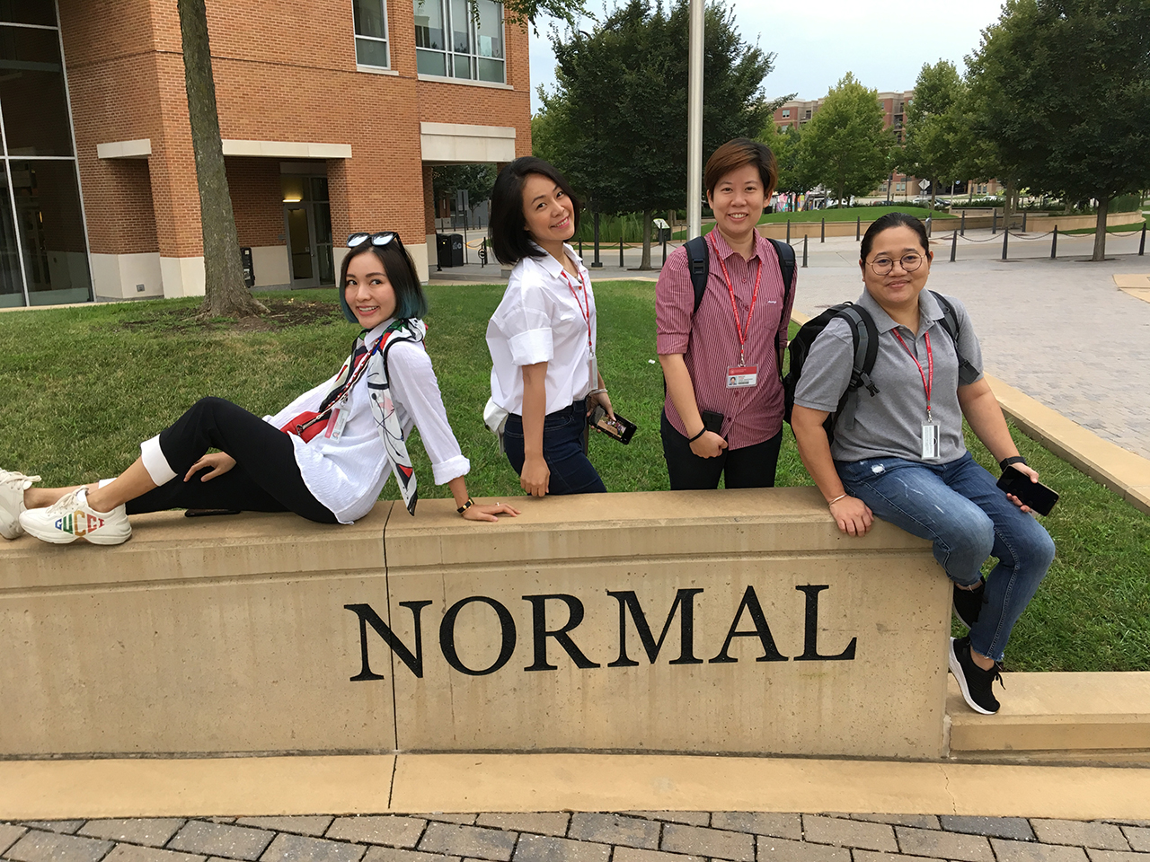 four people seated at a sculpture with the word Normal on it.