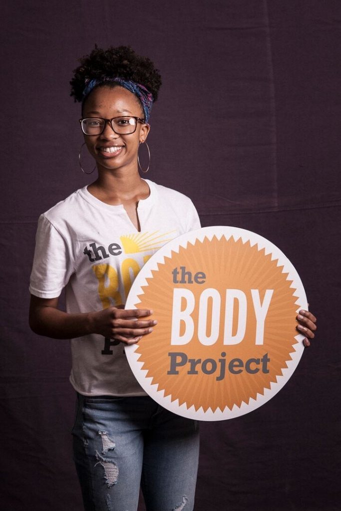 woman holding sign and wearing T-shirt that says The Body Project