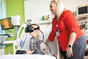 A sick child in a hospital using virtual reality goggles with the founder of the PedsAcademy at the hospital.