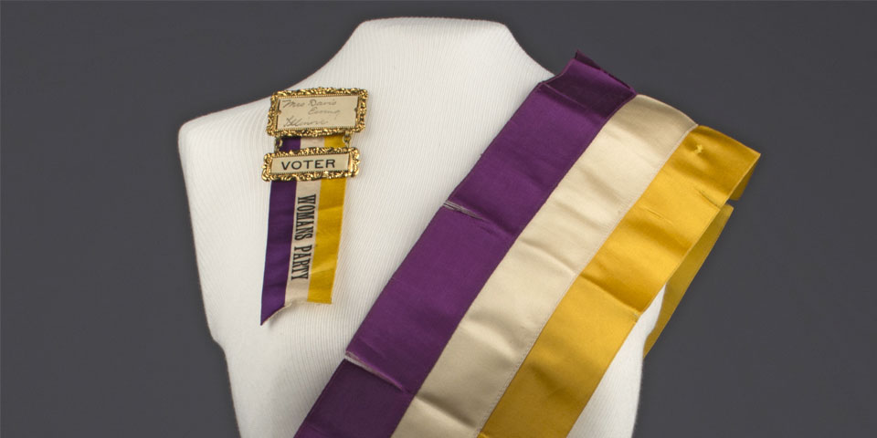White dress form wearing a purple, white, and yellow National Woman's Party sash and ribbon reading "Mrs Davis Ewing Illinois Voter Woman's Party."
