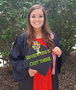 Kenzie Meyer holding a mortarboard that says Adventure is out there.