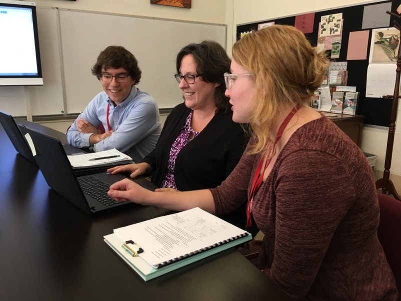 Three people smiling and looking at a laptop