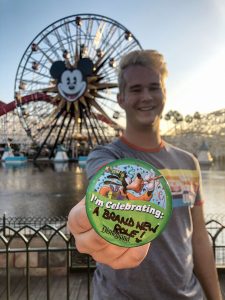 Man standing in front of Mikey Mouse ferris wheel holding a button stating I'm celebrating: A brand new role!